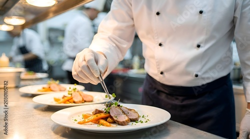 Professional chef in a commercial kitchen using precision tweezers to plate multiple gourmet meat and vegetable dishes on white plates, ensuring consistent high-end restaurant presentation