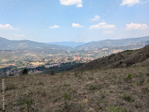 Scenic panoramic high angle view of a beautiful mountain valley and a small rural town nestled between green hills under a bright blue sky, concepts of travel, adventure, and summer vacation