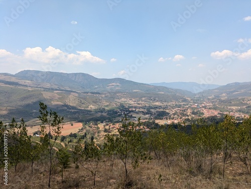 Scenic panoramic high angle view of a beautiful mountain valley and a small rural town nestled between green hills under a bright blue sky, concepts of travel, adventure, and summer vacation