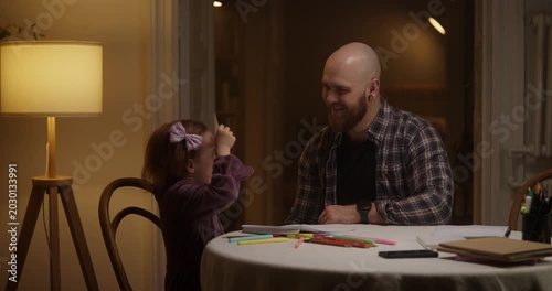 Father and daughter enjoy joyful laughter making colorful crafts at home in the evening glow