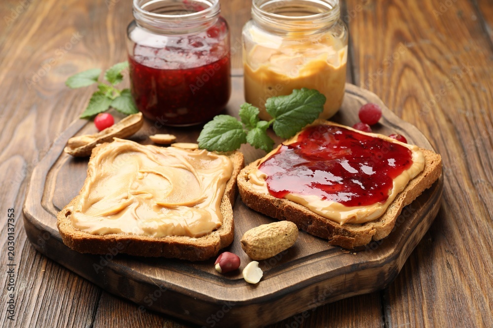 Fototapeta premium Tasty sandwiches with peanut butter, jam, nuts and mint on wooden table, closeup