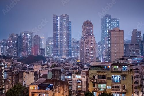 Fotografia Macau, Maco, China : dense residential towers and illuminated apartment buildings disappearing into humid night haze above the urban skyline of Macau