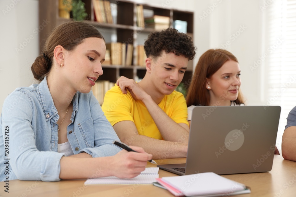 Obraz premium Group of students studying with laptop and notebooks at wooden desk in classroom