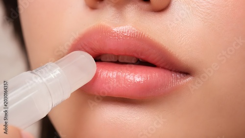 Woman applying moisturizing clear lip balm stick on healthy natural pink lips beauty care close up