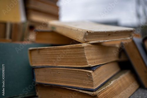 Photos Top view of old antique and secondhand books piled haphazardly on asphalt ground, illustrating a flea market selection, garage sale clutter, or secondary paper waste recycling