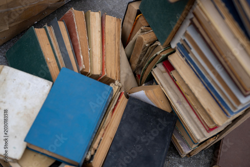 Photos Top view of old antique and secondhand books piled haphazardly on asphalt ground, illustrating a flea market selection, garage sale clutter, or secondary paper waste recycling