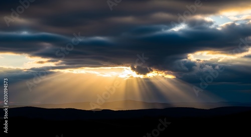 Golden sunbeams break through an ominous cloudscape, illuminating the horizon with a divine glow and offering a moment of natural wonder