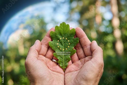 Hands holding green oak leaf with European Union environmental text and stars
