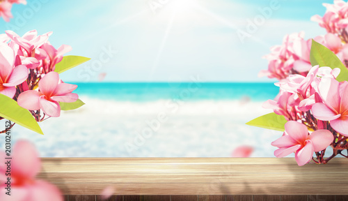 Tropical beach background with pink plumeria flowers and wooden table display, summer product showcase and vacation banner concept.