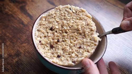 Close-up of failed oatmeal porridge with dry thick texture and compact clump lifted from bowl with spoon. Funny cooking fail, ruined breakfast, swollen oats, bad consistency.
