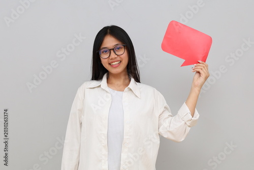 A young Asian woman shows a blank sheet of paper while writing something, smiling looking at the camera, against an isolated white background.