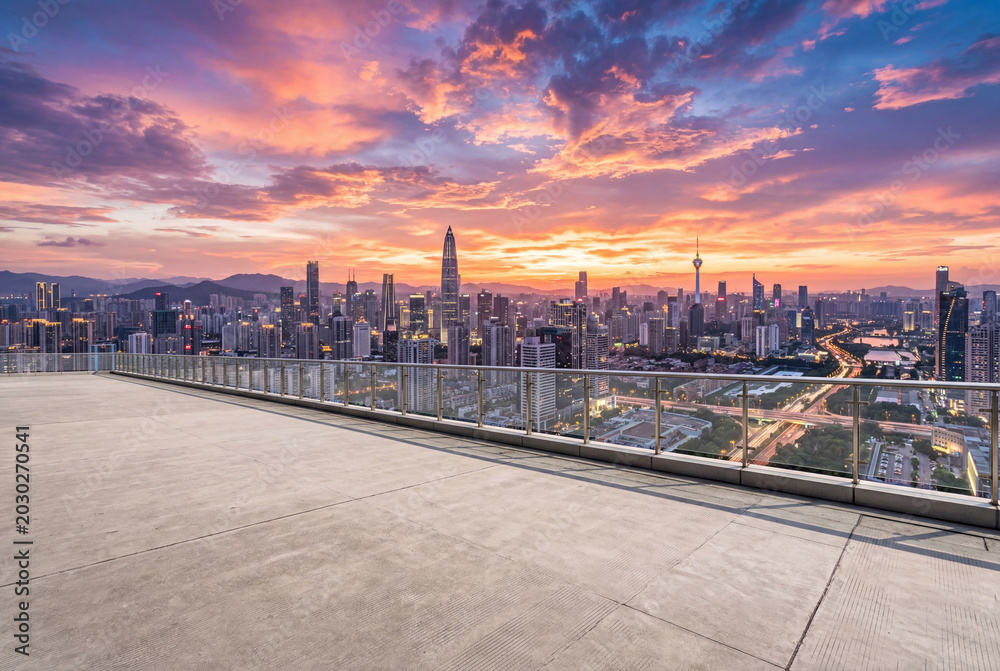 Fototapeta premium Empty concrete rooftop terrace overlooking a modern city skyline at colorful sunset