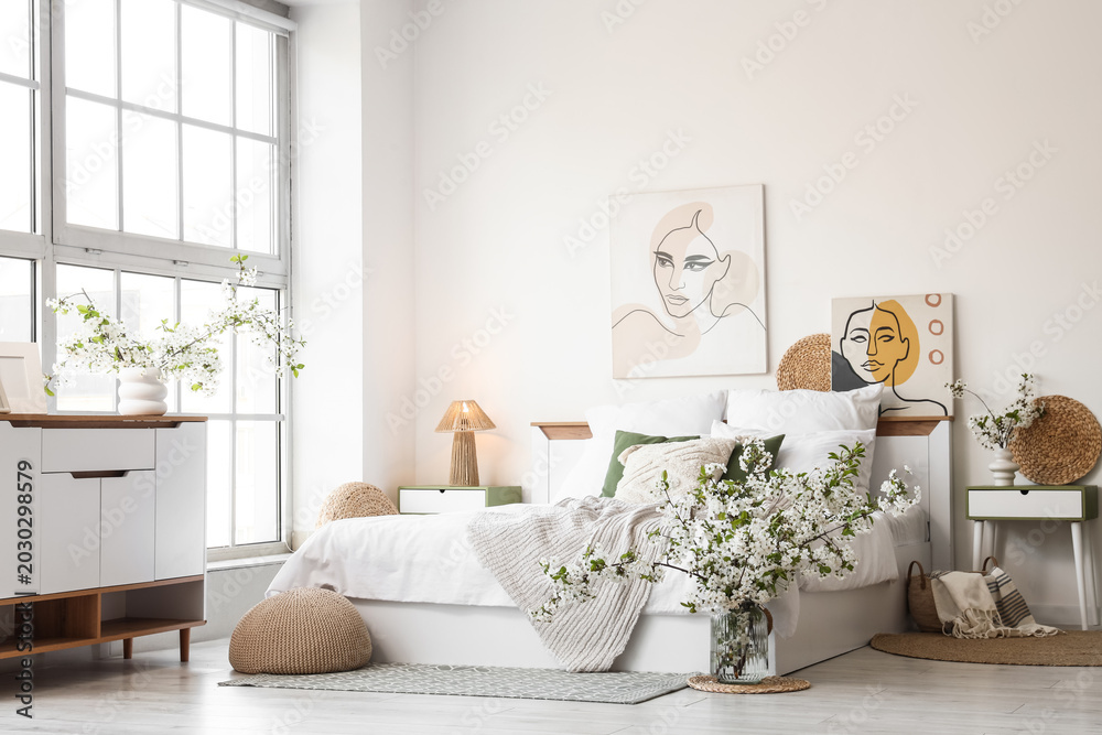 Fototapeta premium Interior of stylish bedroom with bed, commode and vases of blooming tree branches