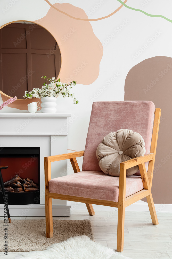 Fototapeta premium Interior of stylish living room with blooming branches in vases, fireplace and armchair