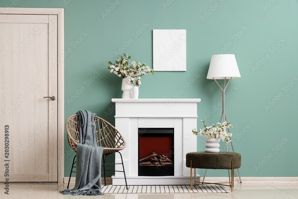 Fototapeta premium Interior of living room with blooming branches in vases, fireplace and armchair