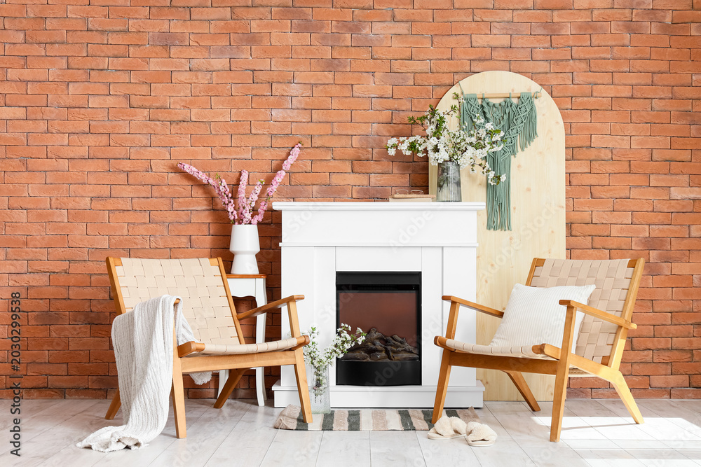 Fototapeta premium Interior of living room with fireplace, armchairs and blooming branches in vases