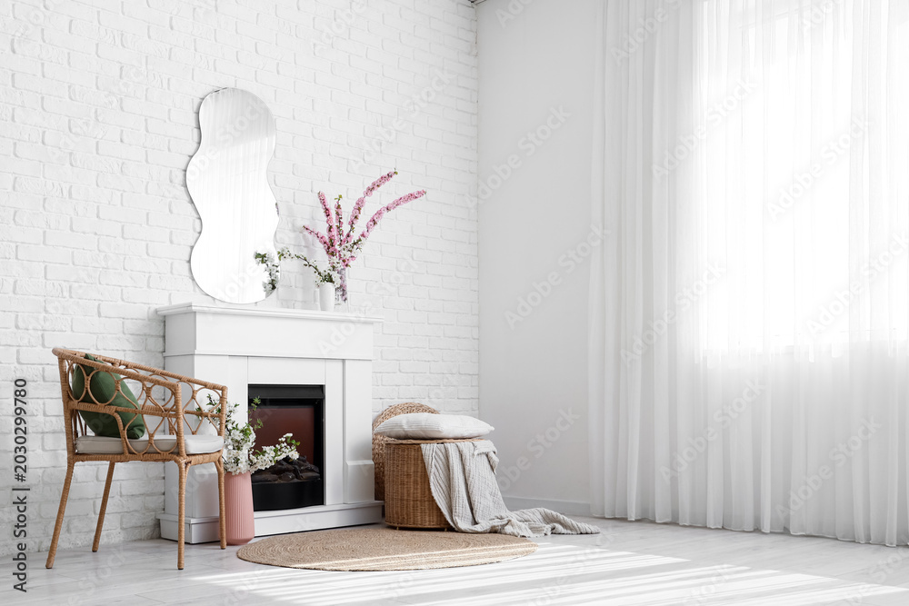 Fototapeta premium Interior of living room with fireplace, armchair and blooming branches in vases