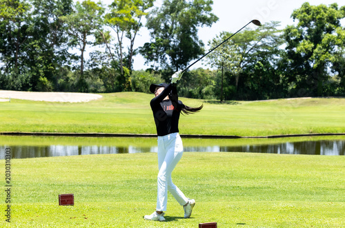 Canvastavla Asian woman golfer swinging on a lush green course with a lake view