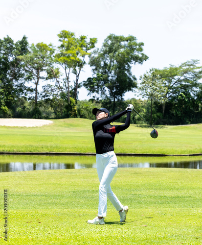 Foto Asian woman golfer swinging on a lush green course with a lake view