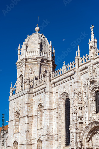 Bild auf Leinwand Lisbon, Portugal - October 11, 2025 - Close-up detail of the intricate Manueline style architecture and spires of the Jeronimos Monastery against a blue sky with the moon