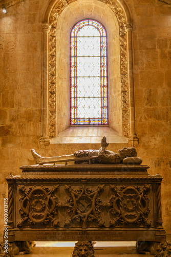 Quadro su tela Lisbon, Portugal - October 11, 2025: An ornate stone tomb illuminated by a stained glass window inside the Jerónimos Monastery
