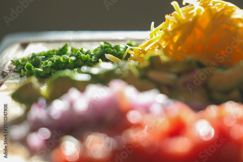 Fresh chopped and grated taco ingredients including tomato, onion, avocado, jalapeno pepper, and cheddar cheese on a cutting board ready to be put in a shell and eaten for dinner. 