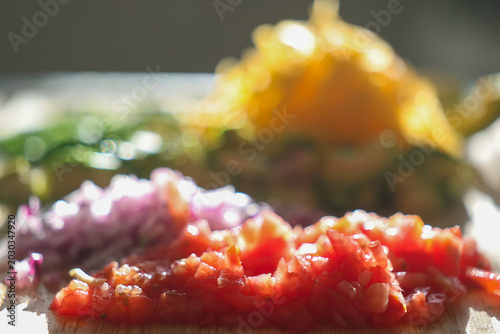 Fresh chopped and grated taco ingredients including tomato, onion, avocado, jalapeno pepper, and cheddar cheese on a cutting board ready to be put in a shell and eaten for dinner. 