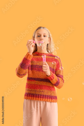 Happy teenager girl blowing soap bubbles on yellow background