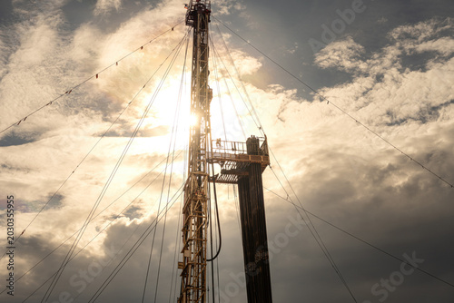 Cuadro en lienzo A low-angle perspective of an onshore oil drilling rig structure and derrick tower with cables against a dramatic sunset sky with clouds
