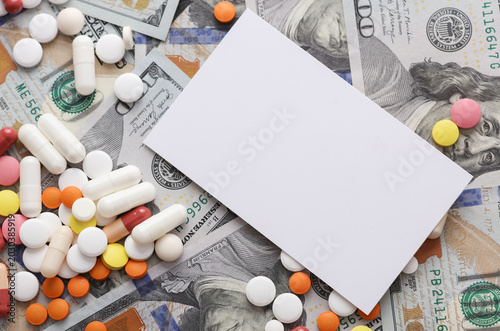 White blank business card and Many different pills on hundred dollar bills. Medicine financing concept