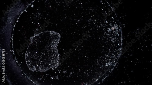 Top-down macro view of silver particles swirling in black liquid, mimicking a deep space galaxy with stars. Cinematic high-contrast abstract texture for science and meditation visuals.