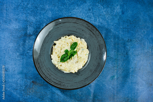 Slika na platnu Delicious creamy risotto dish with basil on a blue tablecloth