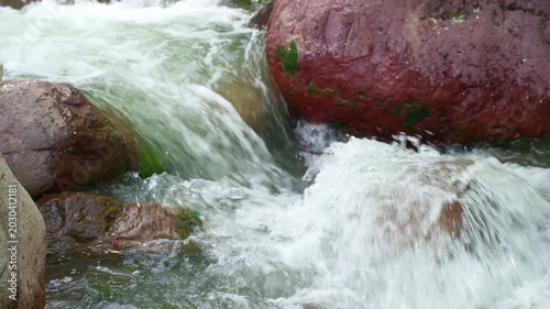 Close up of fast mountain river stream flowing between large rocks, with rushing clear water in natural outdoor landscape.