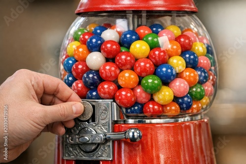 A person holding a gum ball machine filled with colorful gumballs, ready to dispense treats