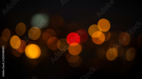 abstract, blurred photograph featuring a bokeh effect with circular light patterns. The layout is predominantly dark with scattered, out-of-focus lights in various colors, including yellow, red, and o