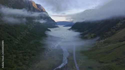 Aerial view of a dramatic Norwegian valley with low clouds, winding river and a road at dawn