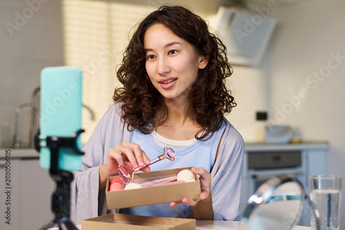 Quadro su tela Asian young woman presenting beauty tools during livestream, holding skincare products for influencer marketing and social media promotion