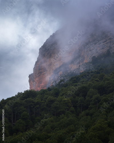 Clouds Embrace the Rocky Peak of Vall De Cabo in Enchanting Catalonia