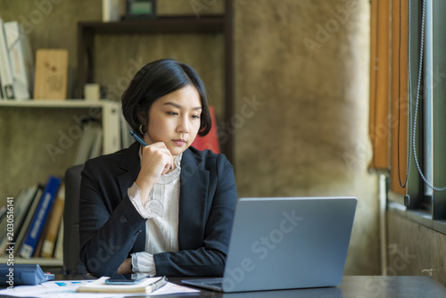 Serious Asian Businesswoman Thinking and Working with Laptop at Desk in Modern Office.