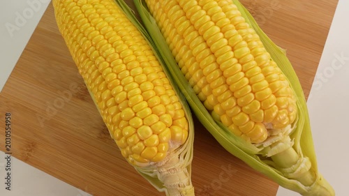 Fresh corn cobs on wooden board rotate.