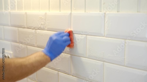 Thoroughly cleaning the grout between tiles. Manually cleaning stains on white tiles. Close-up of a gloved hand cleaning white tiles. A variety of tile cleaning products. The problem of cleaning.