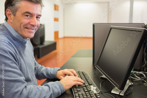 Fotografie Man in blue-gray sweater typing on full keyboard at training room with monitor,