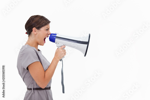 Konstfotografi Woman shouting into megaphone, standing by white backdrop in gray dress, thin da