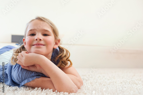 Foto School-age girl lying on plush white shag carpet at home, wearing blue top, dark