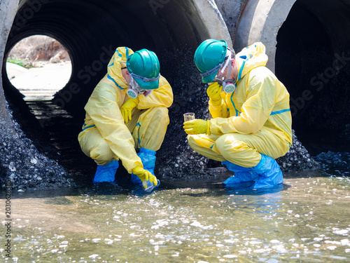 Tableau sur toile Environmental engineers in chemical protective suits are collecting samples of contaminated water, ecologically and industrially, from nearby areas for testing