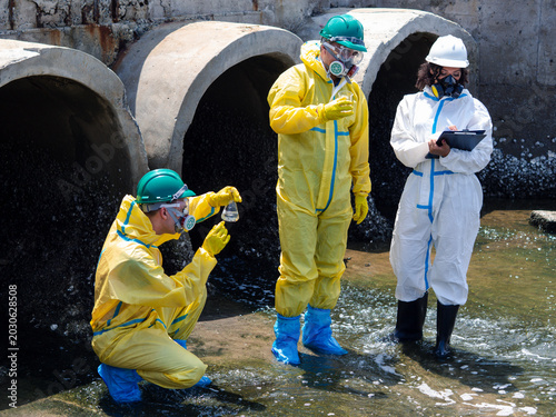 Tableau sur toile Environmental engineers in chemical protective suits are collecting samples of contaminated water, ecologically and industrially, from nearby areas for testing
