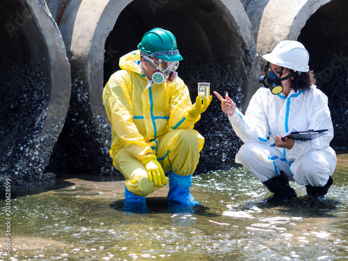 Tableau sur toile Environmental engineers in chemical protective suits are collecting samples of contaminated water, ecologically and industrially, from nearby areas for testing