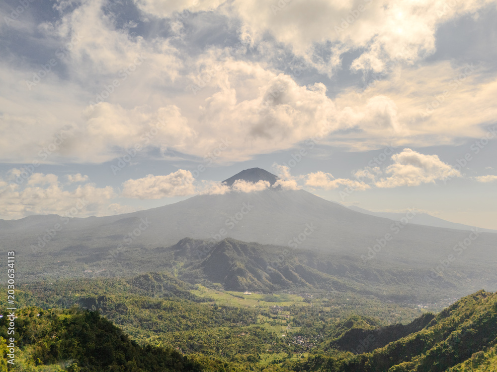 Fototapeta premium Volcanic Mountain Over Green Valley Under Cloudy Sky