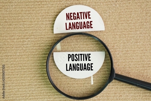 Magnifying glass and paper with the words Positive vs Negative Language. Negative language reflects a negative attitude and mood, whereas positive language communicates a supportive, confident