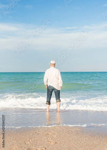 Rear view of senior man standing in sea water looking at horizon on peaceful beach vacation